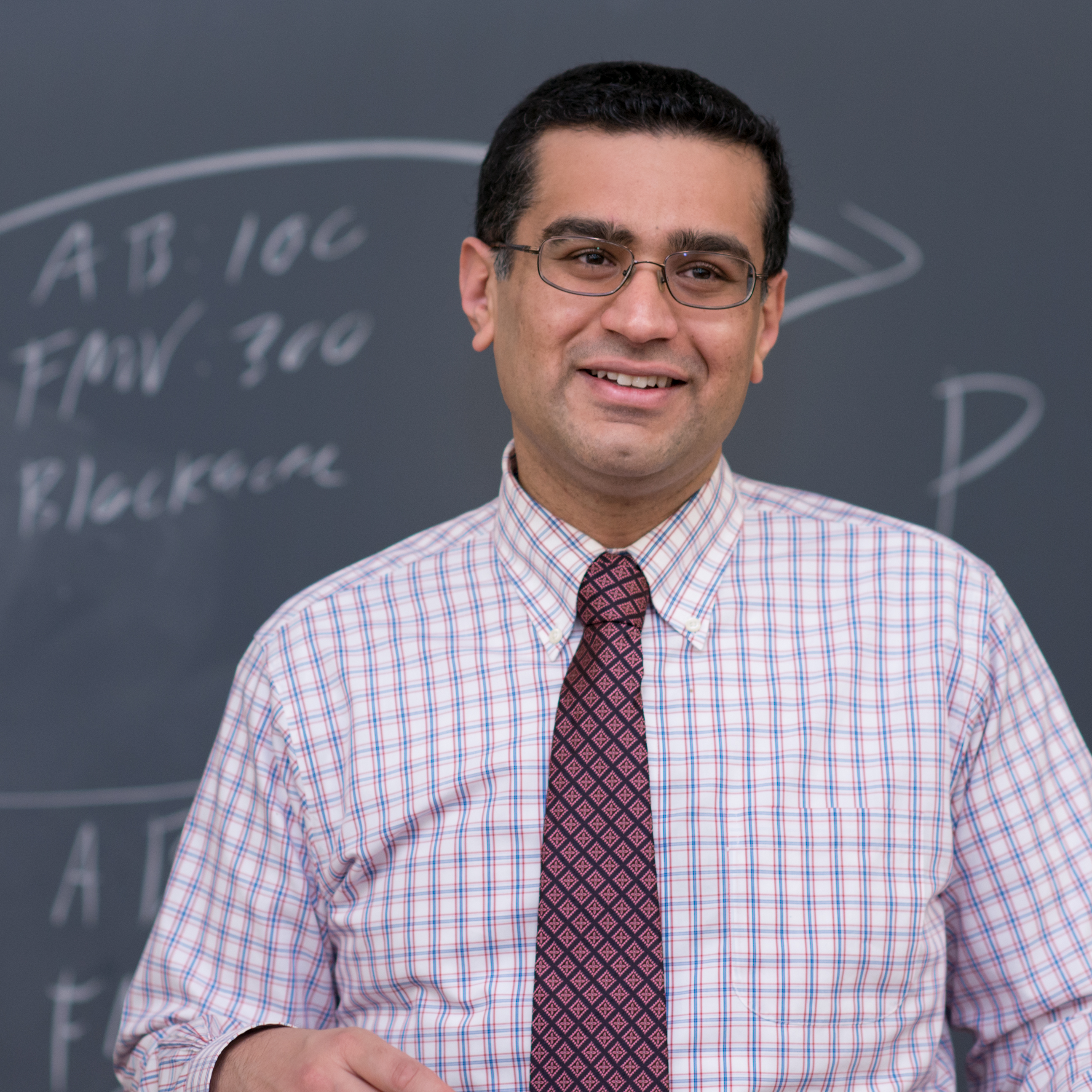 Photo of Professor Andy Grewal standing in front of a chalk board